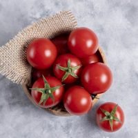 A wooden bowl full of fresh juicy red tomatoes placed on stone table . High quality photo